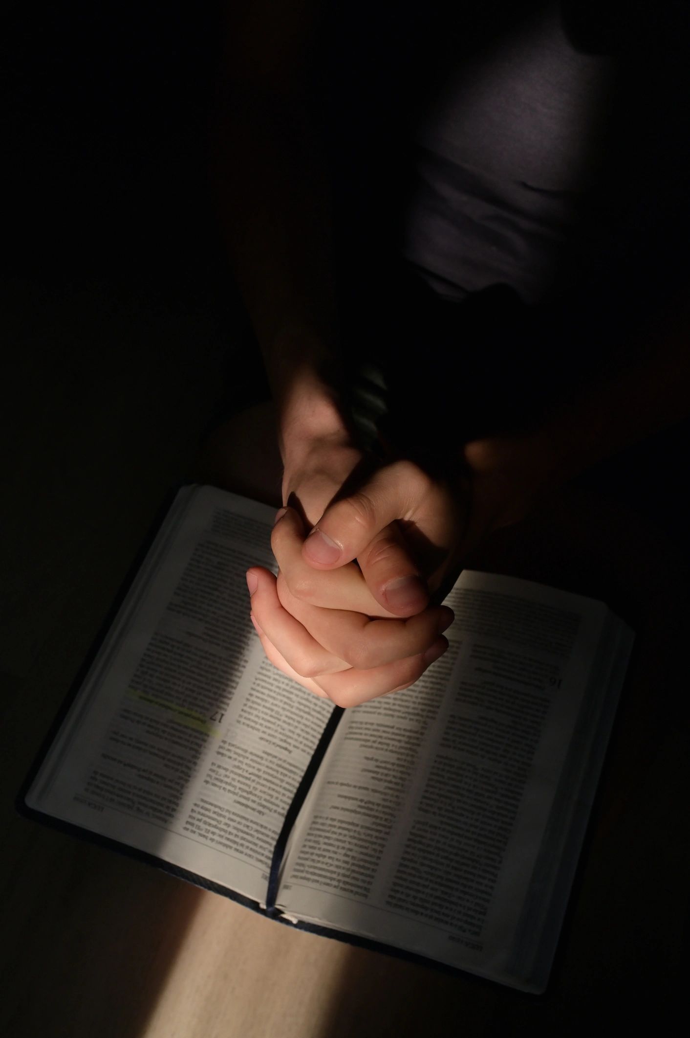 Young man praying with hands clasped in sunlight