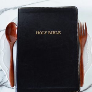 Holy bible book on empty plate with spoon and fork on white table