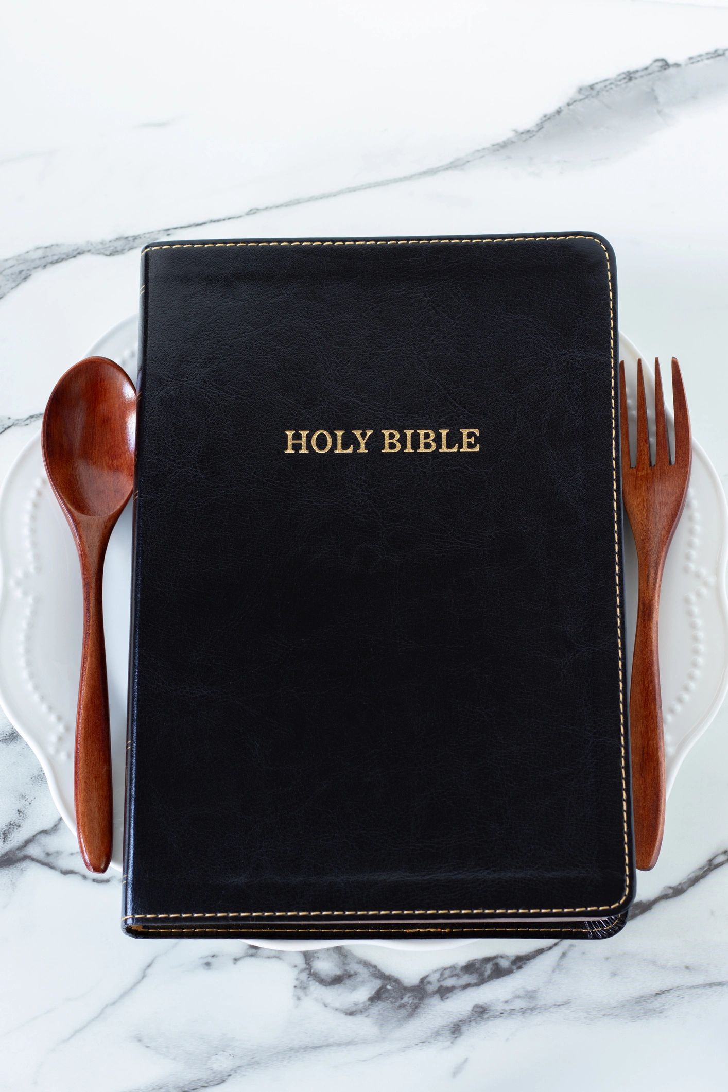 Holy bible book on empty plate with spoon and fork on white table